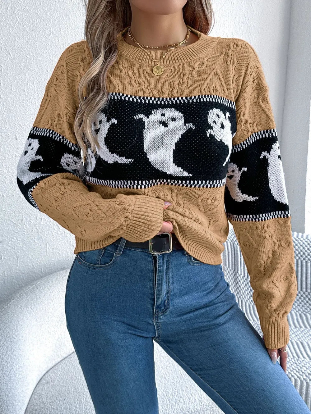 A woman wears a brown, black, and white ghost-patterned long-sleeve sweater with jeans.