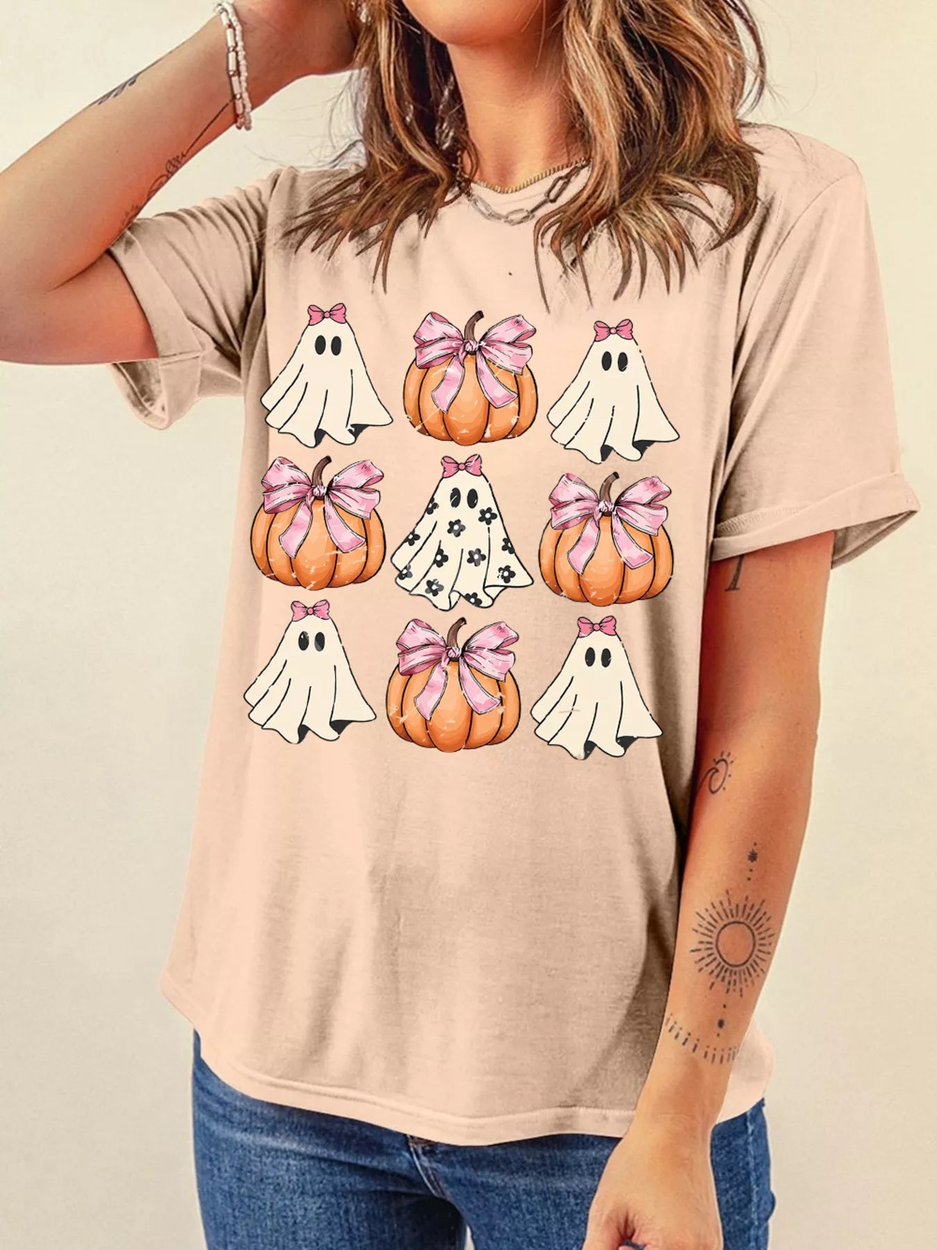 A woman wears a Halloween graphic t-shirt with ghosts and pumpkins with pink bows.