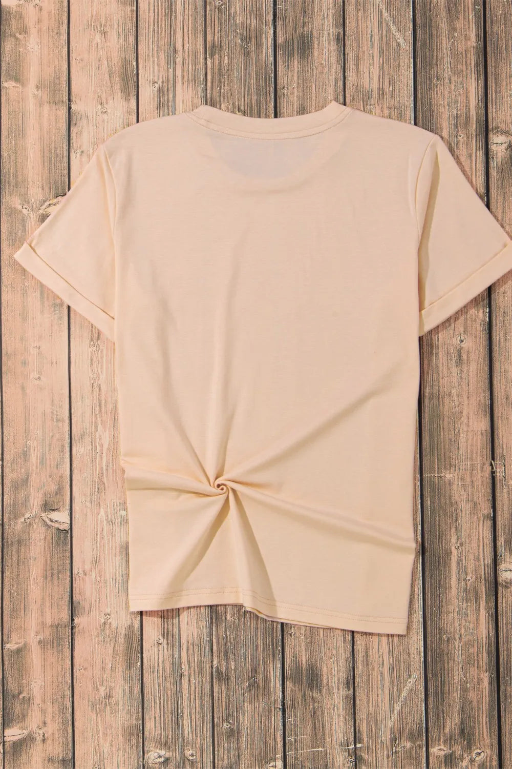 A light orange short-sleeve t-shirt with a knotted hem is displayed on a wooden background.