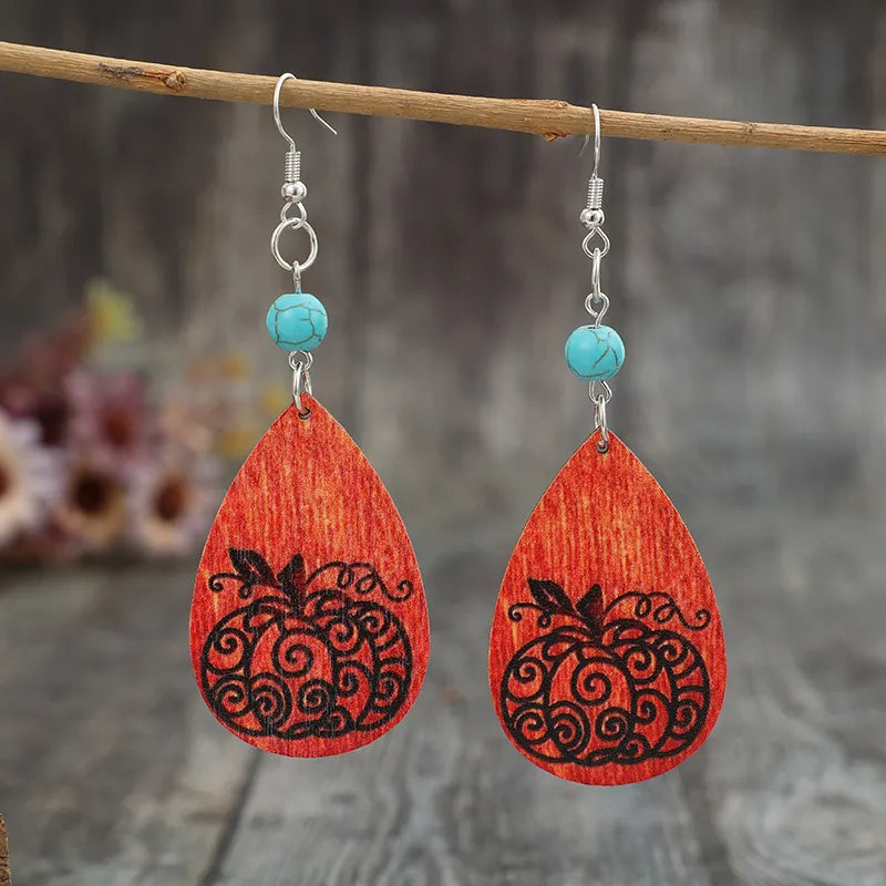 Turquoise wooden pumpkin teardrop earrings hang from a branch.
