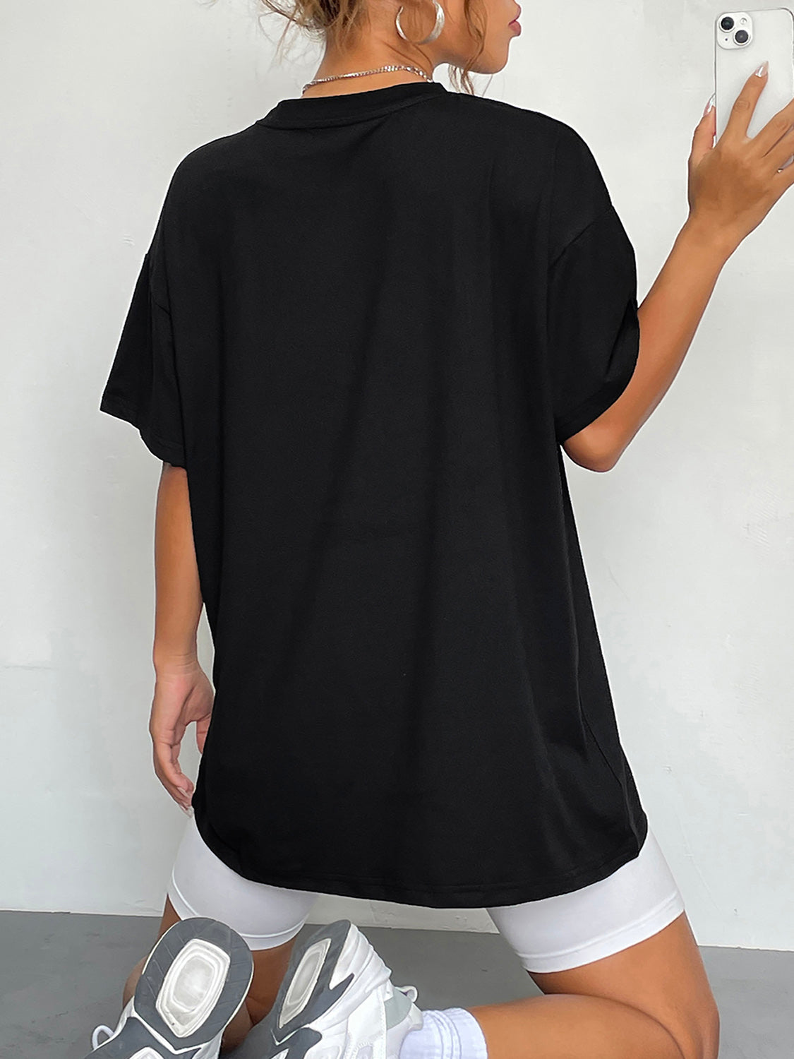 A woman from behind wearing a black round neck short sleeve t-shirt and white shorts.