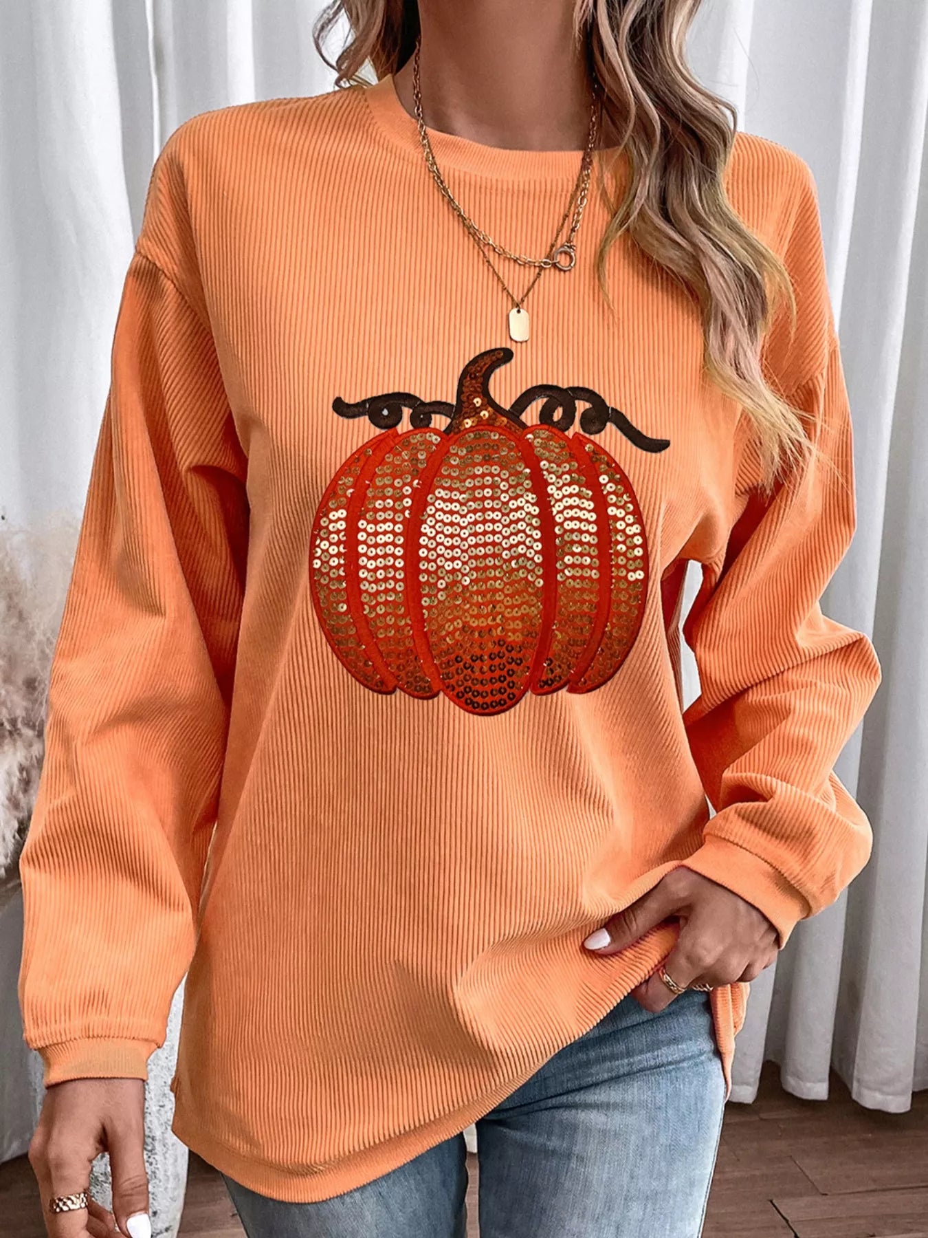 An orange ribbed sweatshirt with a sequined pumpkin design.