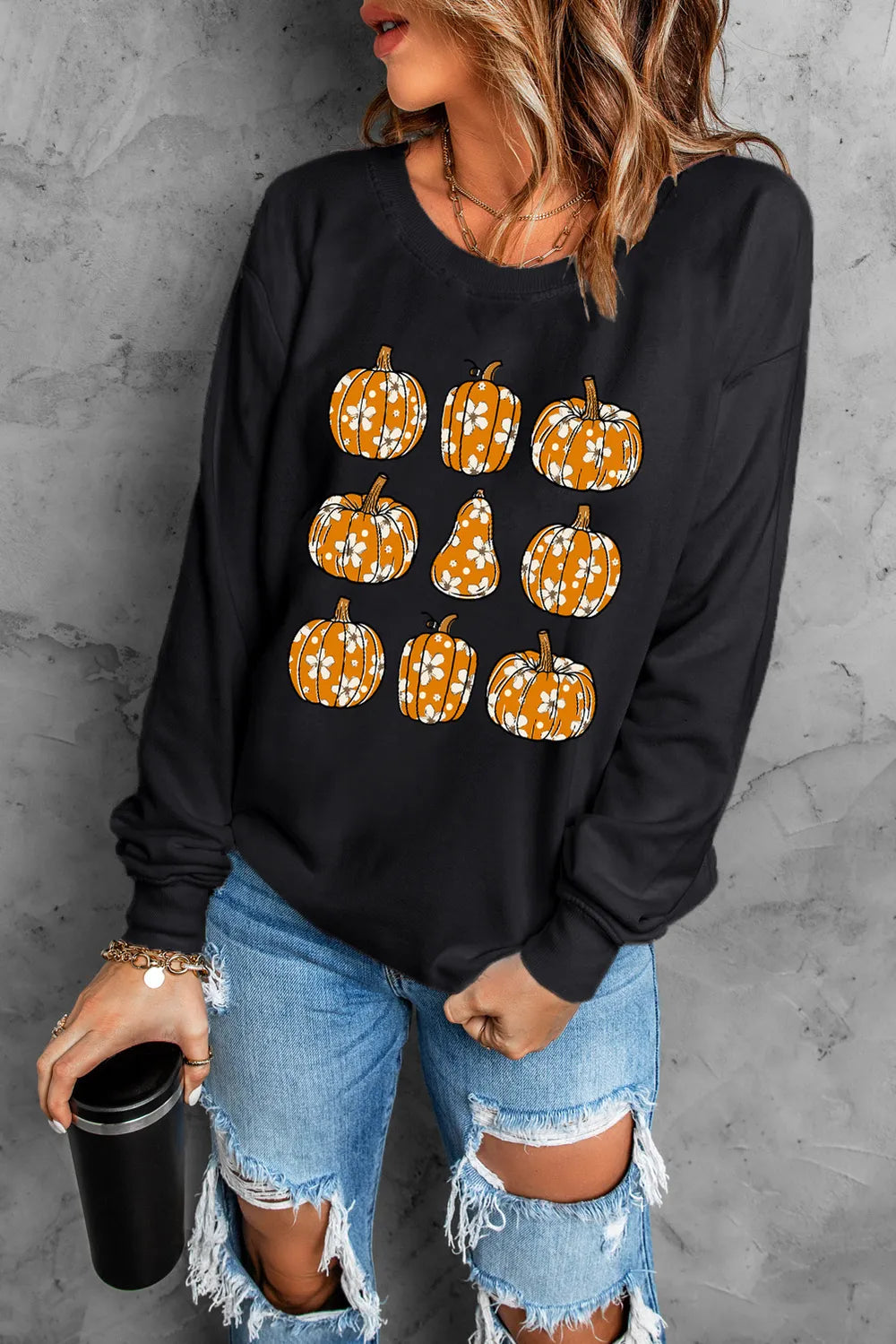 A woman wears a black long-sleeve sweatshirt with pumpkin graphics and ripped jeans.
