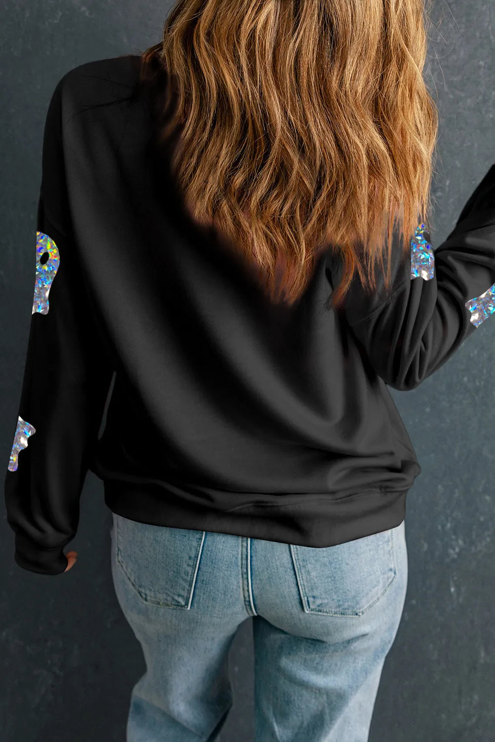 A woman from behind wears a black long-sleeve sweatshirt with iridescent ghost appliques.