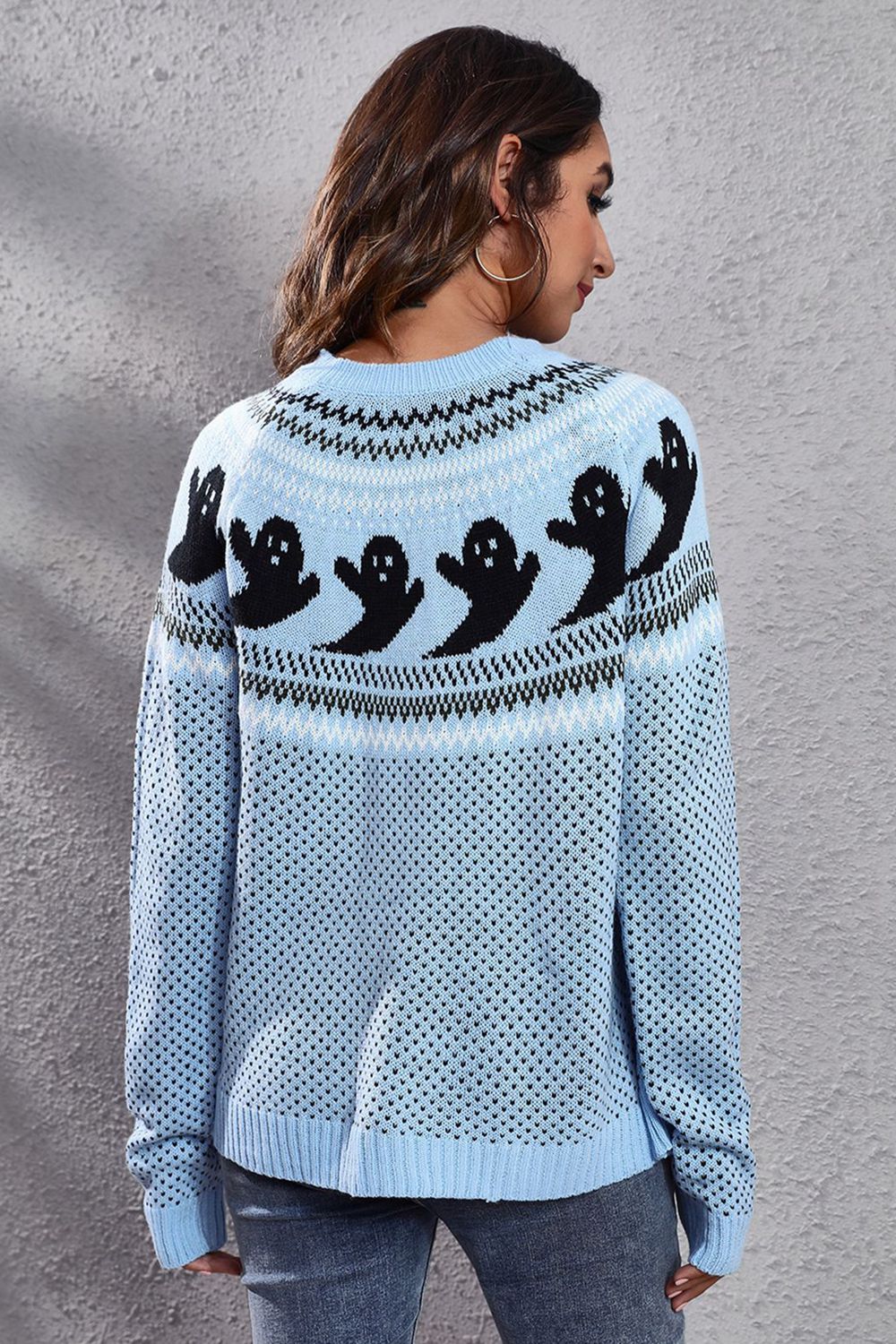A woman models a light blue, long-sleeve sweater with a ghost pattern on the back.