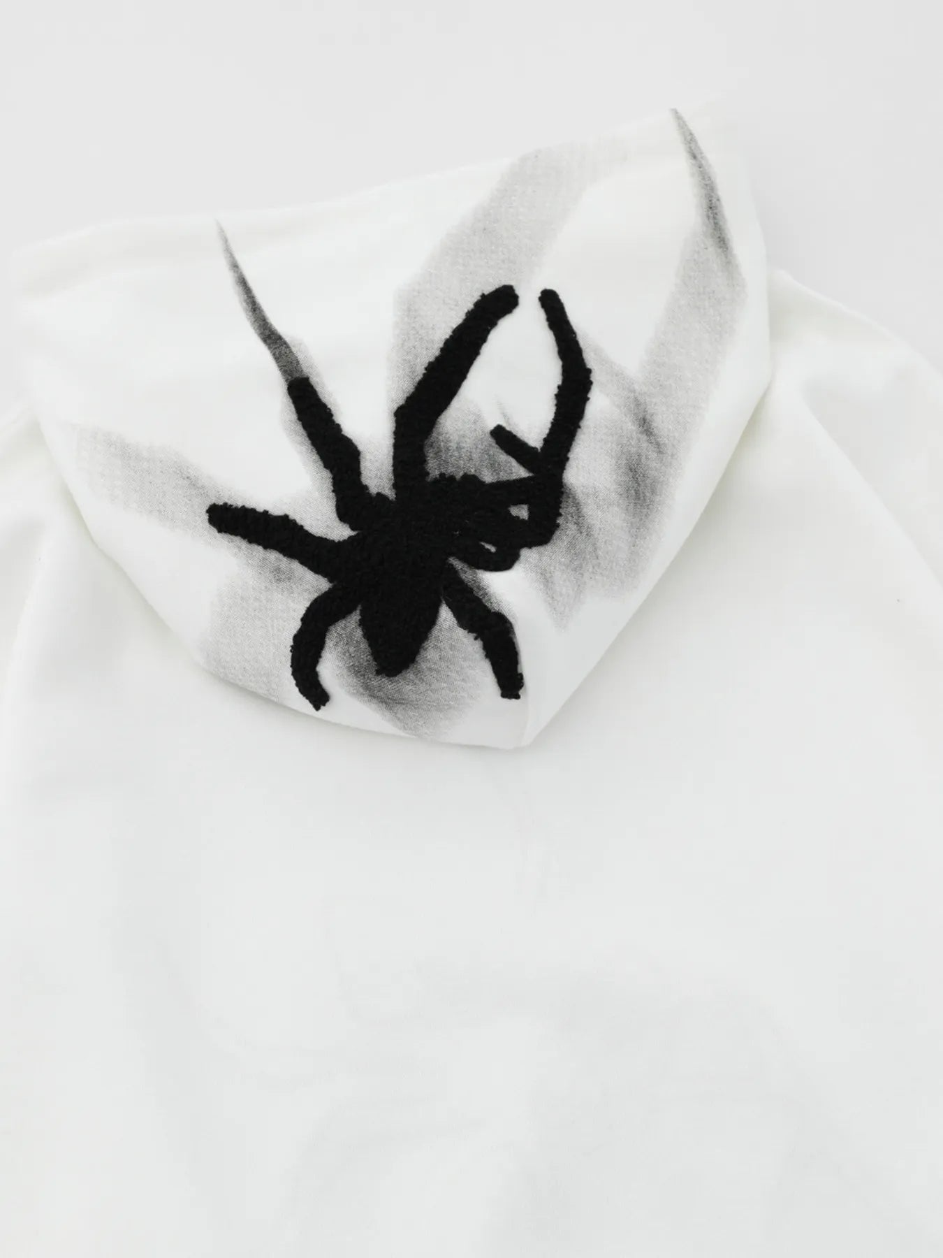White oversized hoodie with a black spider graphic on the hood.