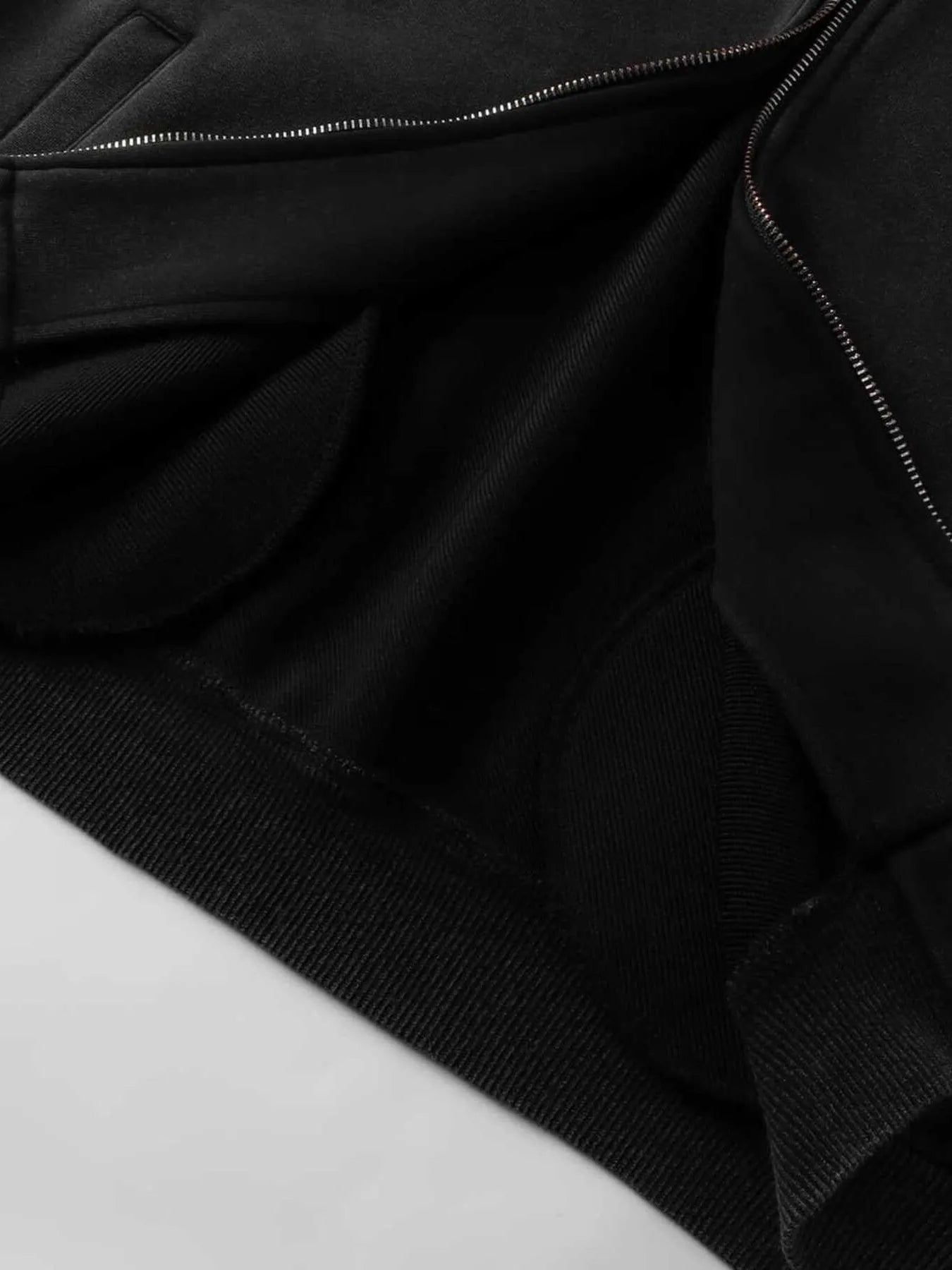 Black zip-up hoodie with ribbed cuffs and hem, showing the zipper and inner fabric.