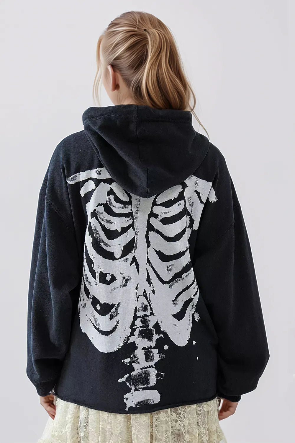 A person from behind wears a black skeleton zip-up hoodie over a lace skirt.