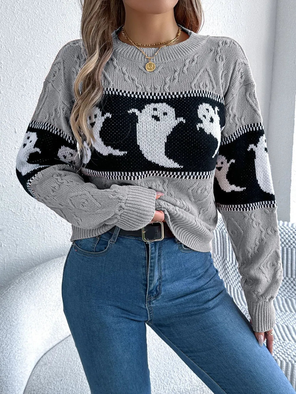 A woman wears a gray, long-sleeve sweater with a black and white ghost pattern.