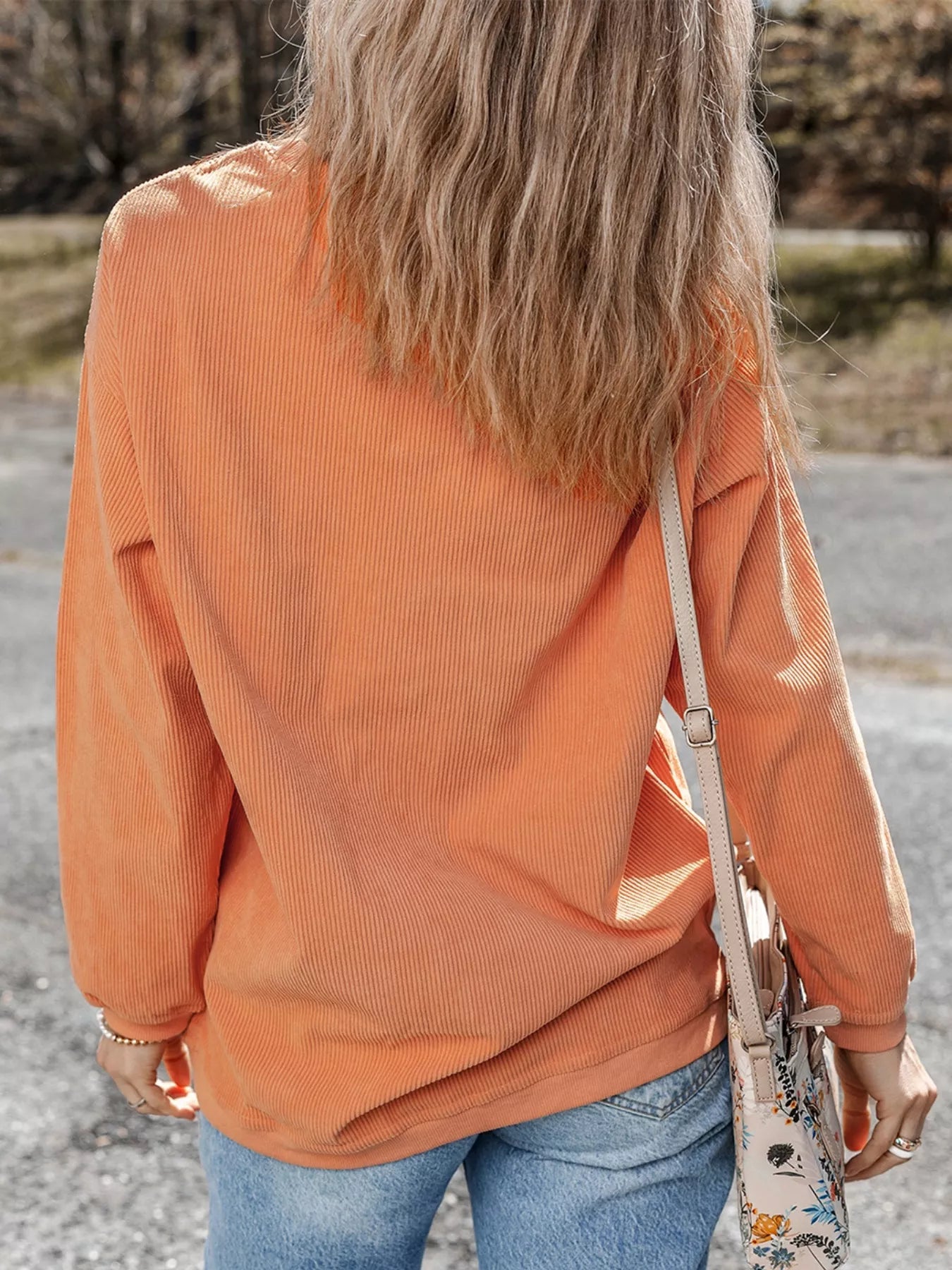 A woman from behind wears an orange ribbed round neck sweatshirt and jeans.
