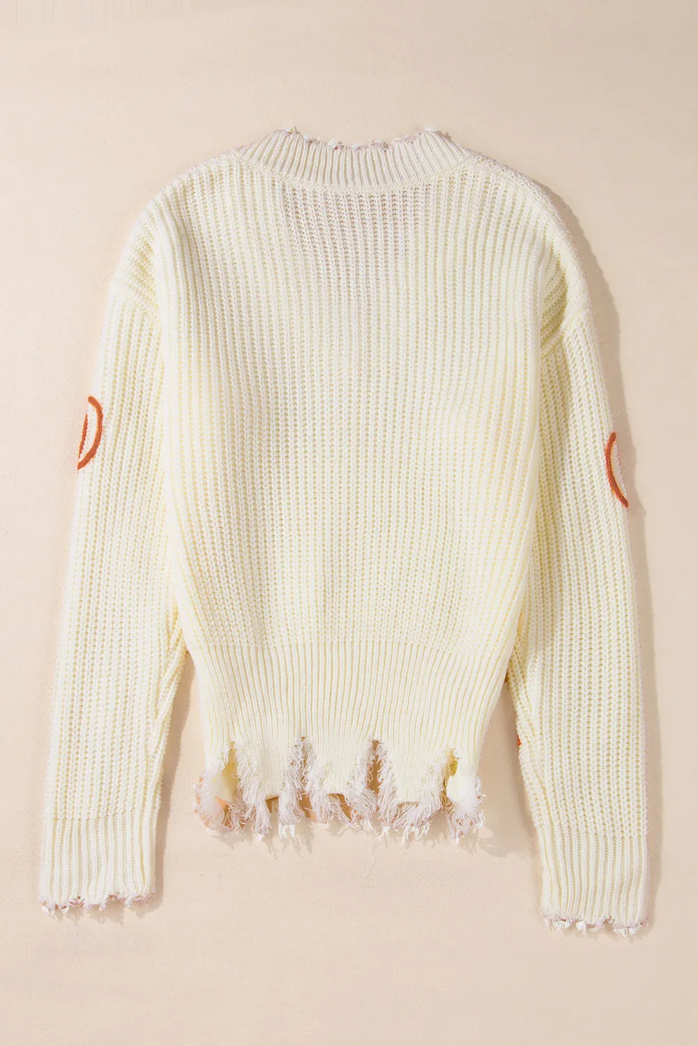 A cream-colored, distressed sweater with pumpkin accents on the sleeves.