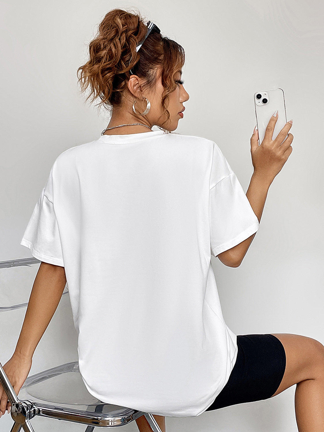 A woman from behind wears a white round neck short sleeve t-shirt.