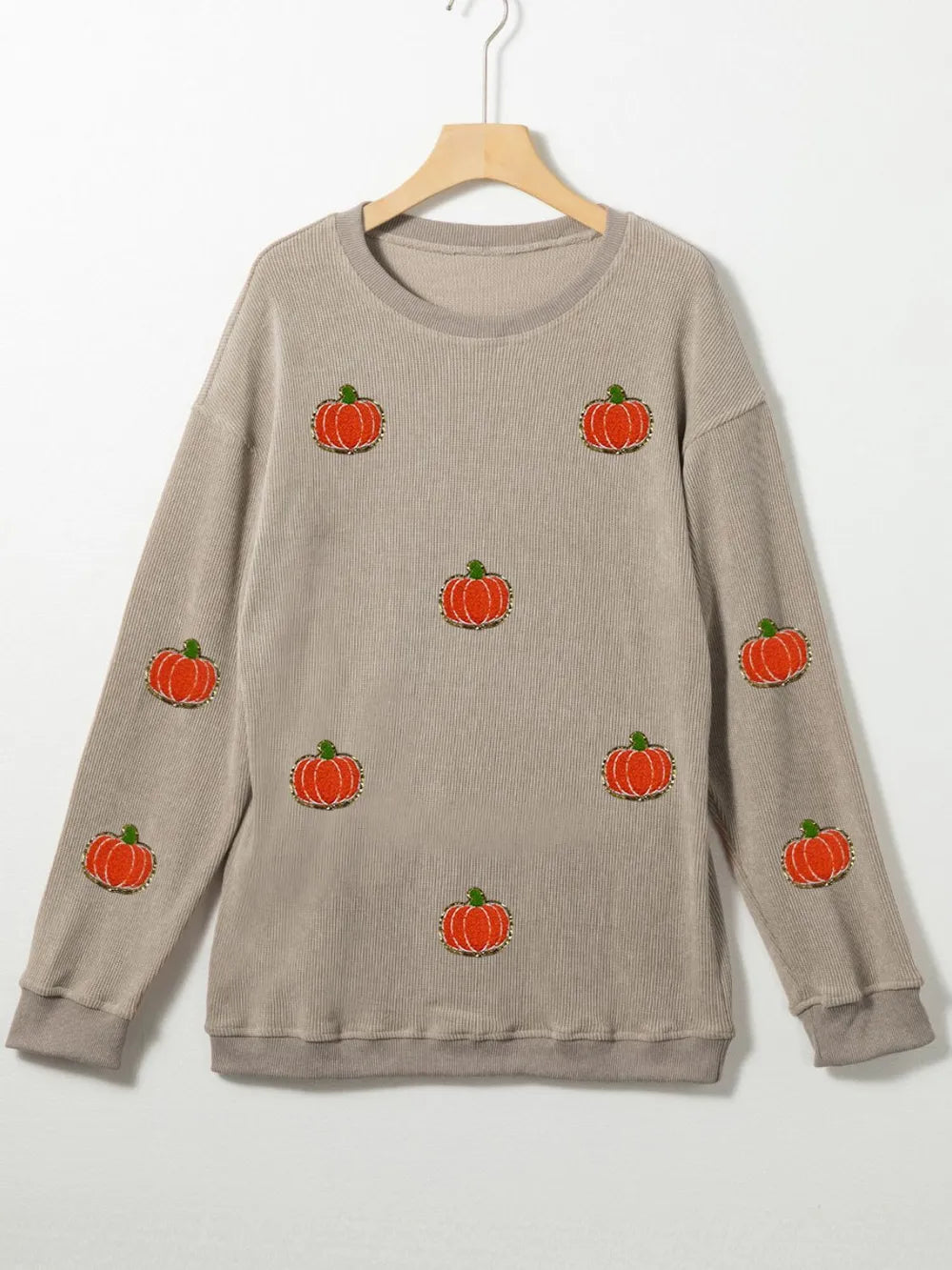 A beige long-sleeve sweatshirt with multiple orange pumpkin appliques.