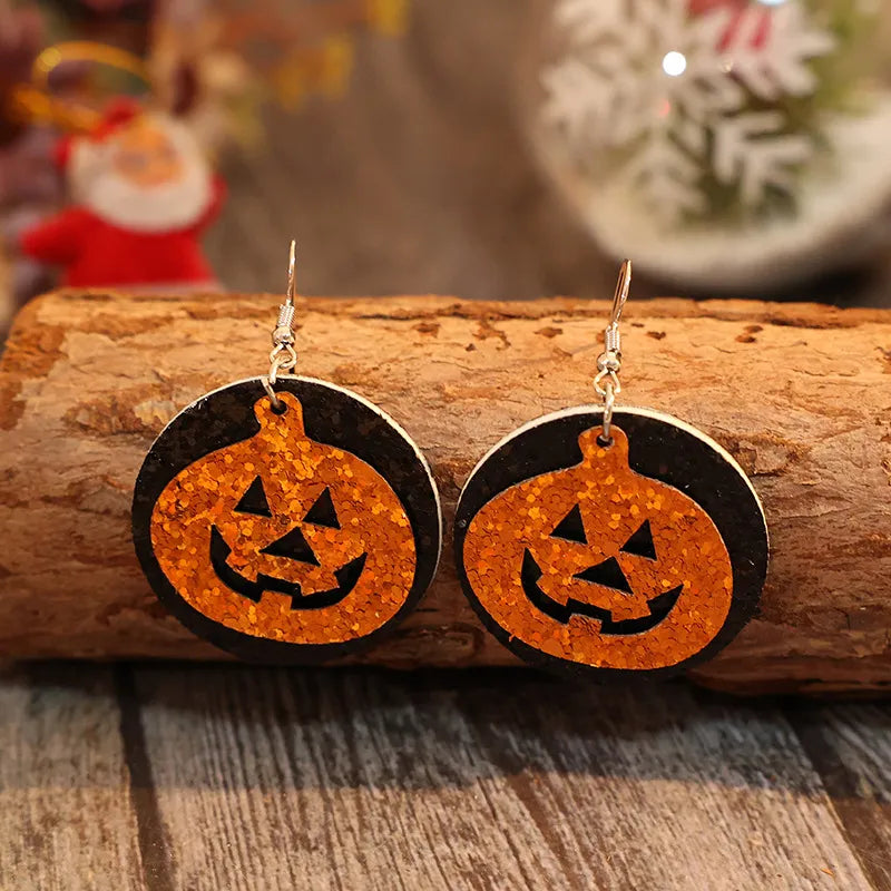 A pair of orange glitter pumpkin earrings with black accents rests on a wooden log.