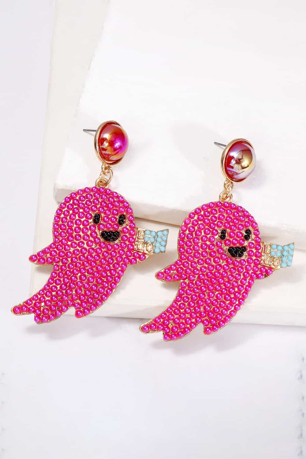 Two pink, ghost-shaped dangle earrings with black faces and light blue accents.
