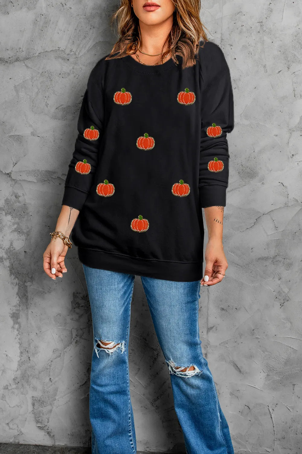 A woman wears a black long-sleeve sweatshirt with pumpkin designs and ripped jeans.