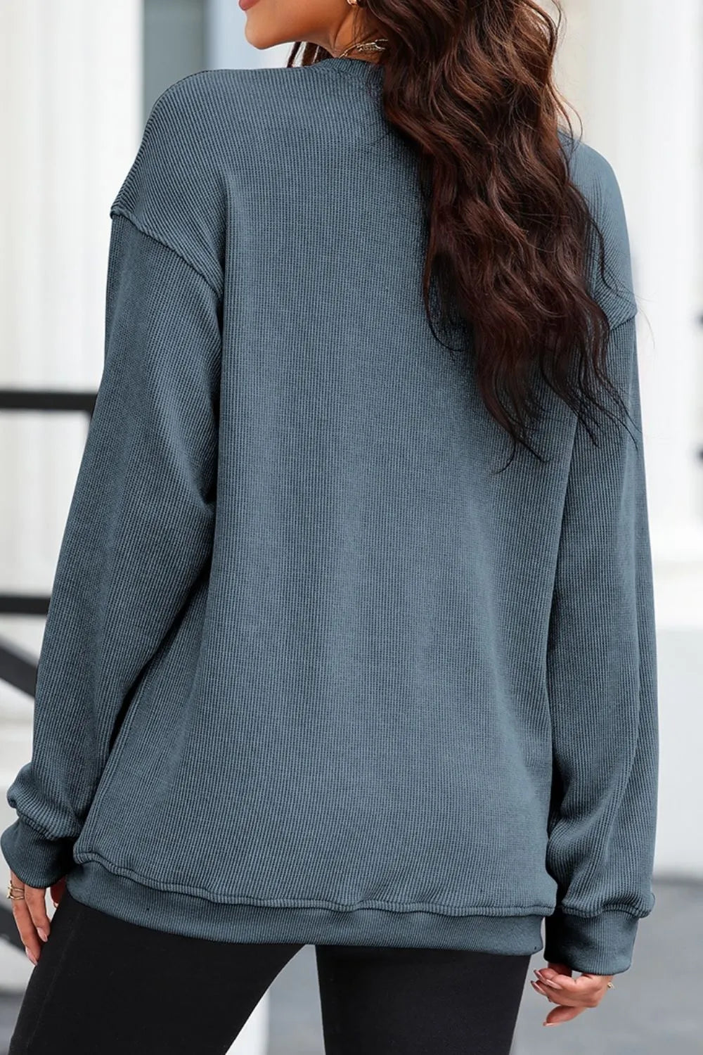 A woman from behind wears a blue ribbed long-sleeve sweatshirt and black pants.