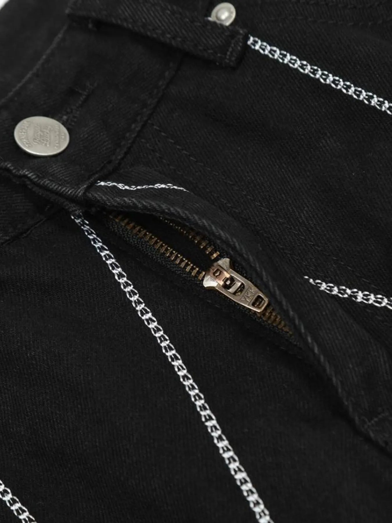 Close-up of black jeans with white chain embroidery and a partially unzipped fly.