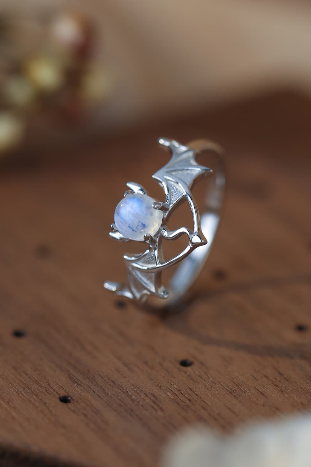 Sterling silver bat-wing ring with a central moonstone, resting on a wooden surface.