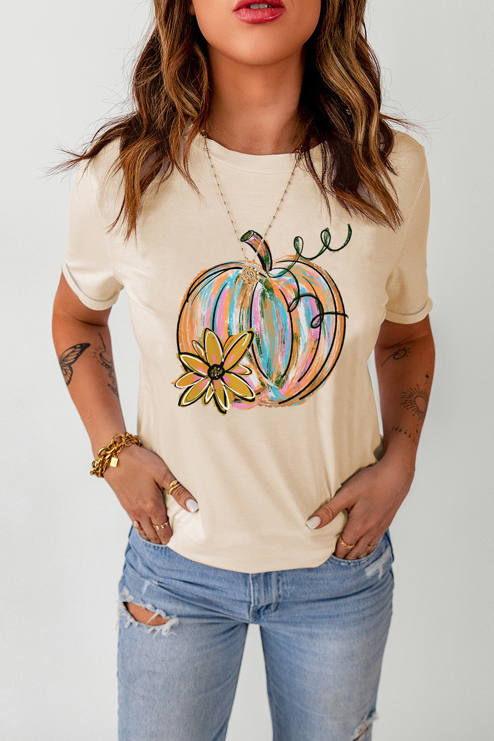 A woman wears a cream-colored t-shirt with a colorful pumpkin graphic.