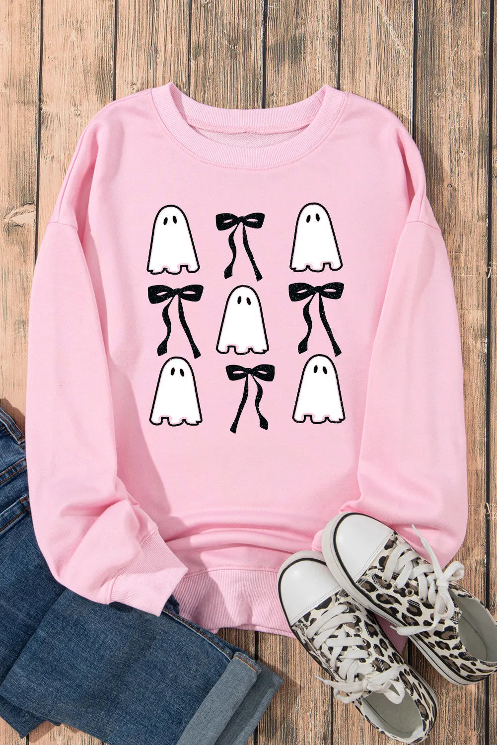 Pink long-sleeve sweatshirt with ghost and bow graphics, paired with jeans and sneakers.