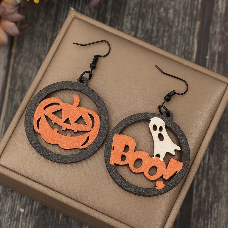 Hollow pumpkin and "Boo!" ghost wooden earrings on a brown display.