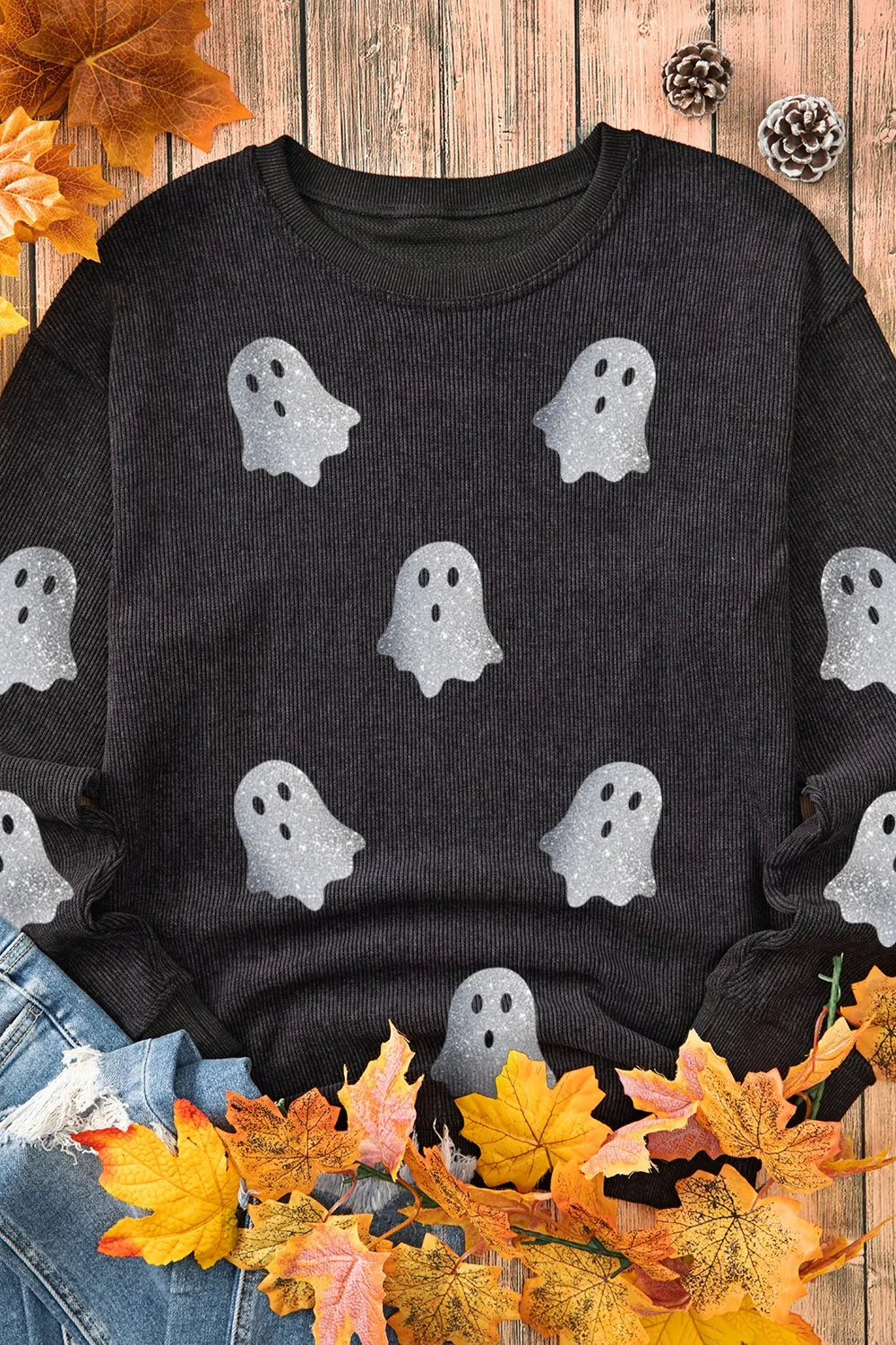 Black long-sleeve sweatshirt with glitter ghost print, styled with jeans and autumn leaves.