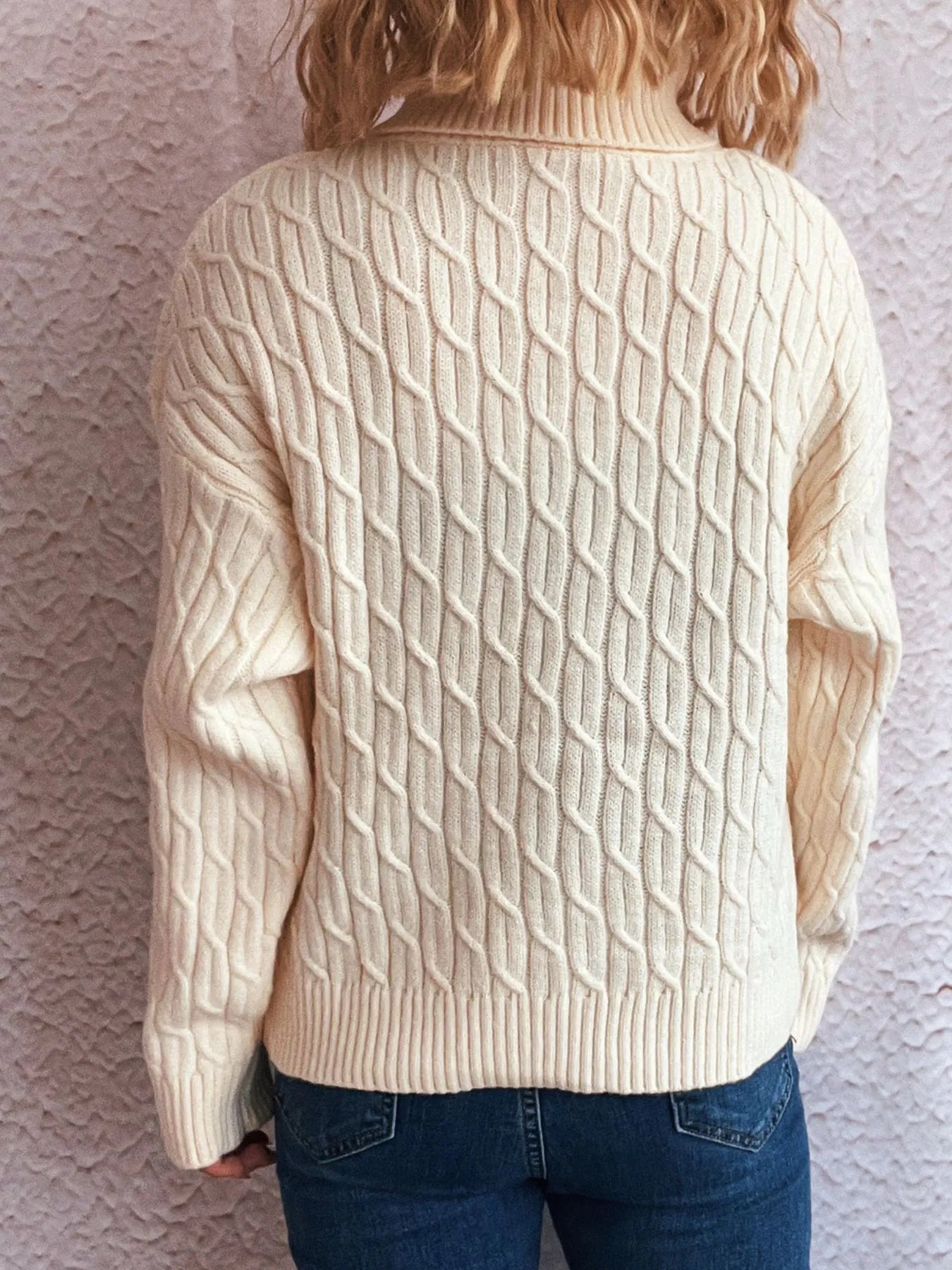 Cream cable-knit turtleneck sweater with long sleeves.