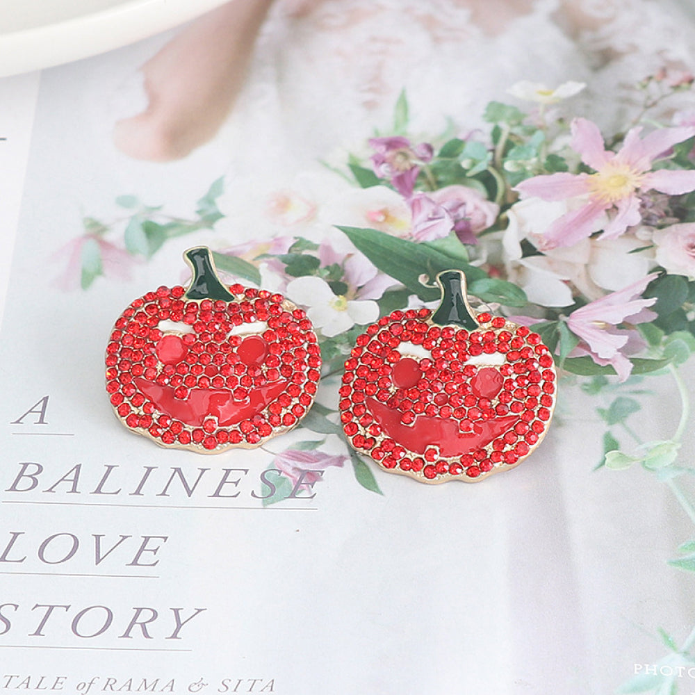 Two red rhinestone pumpkin earrings with black stems are displayed on a floral background.