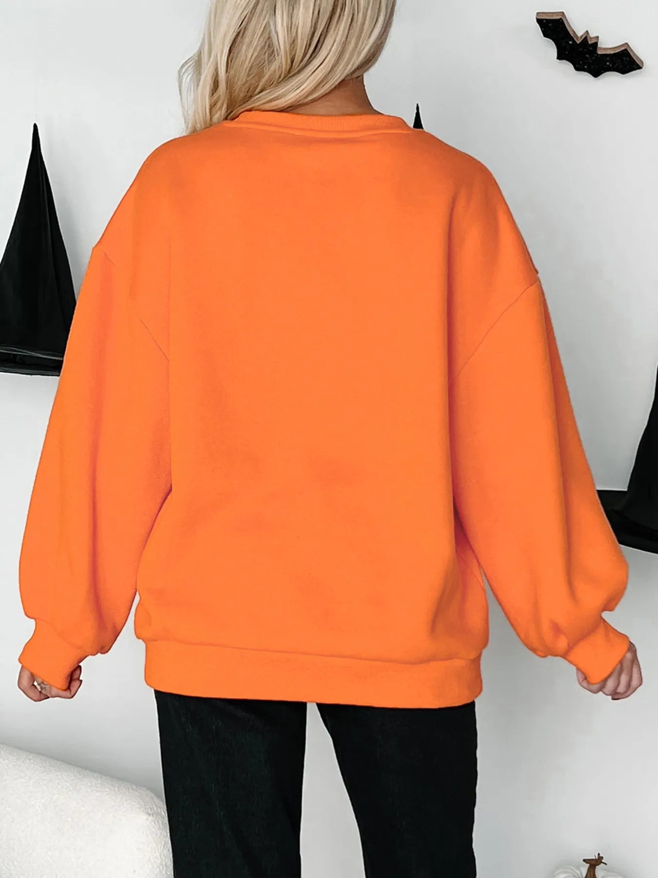 A blonde woman from behind wears an orange Halloween skeleton pumpkin sweatshirt.