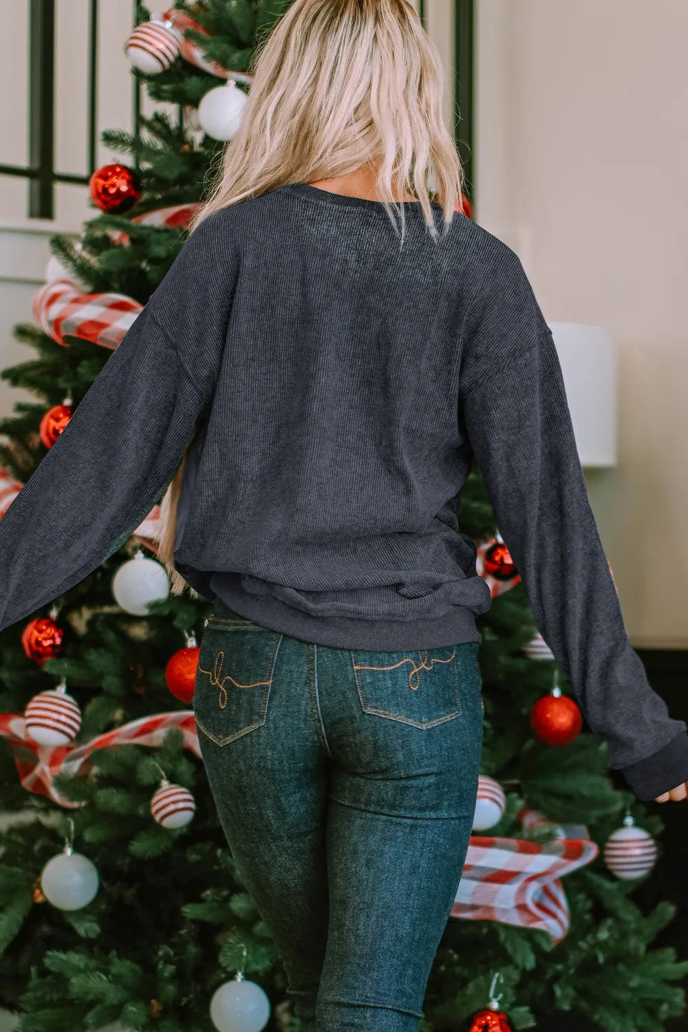 Woman in a dark gray ribbed sweatshirt and jeans, facing away from the camera.