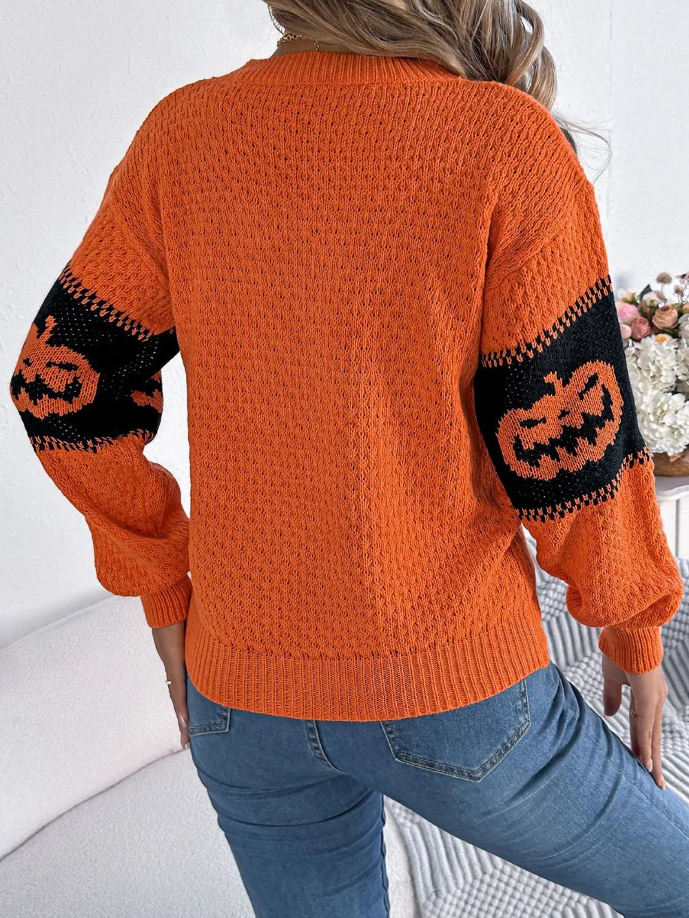 Orange long-sleeve sweater with black pumpkin designs on the sleeves.