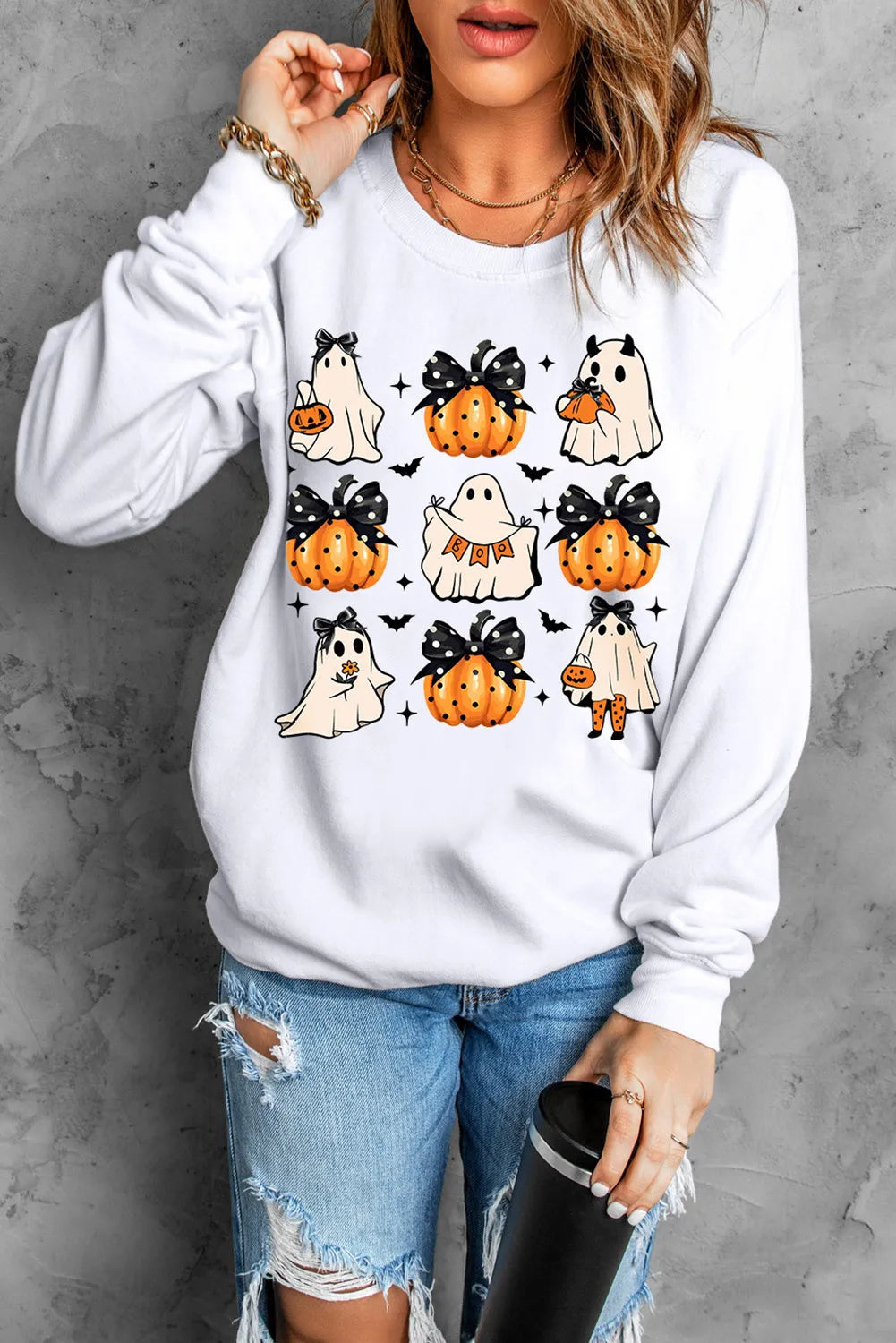 A woman wears a white long-sleeve sweatshirt with pumpkin and ghost graphics.