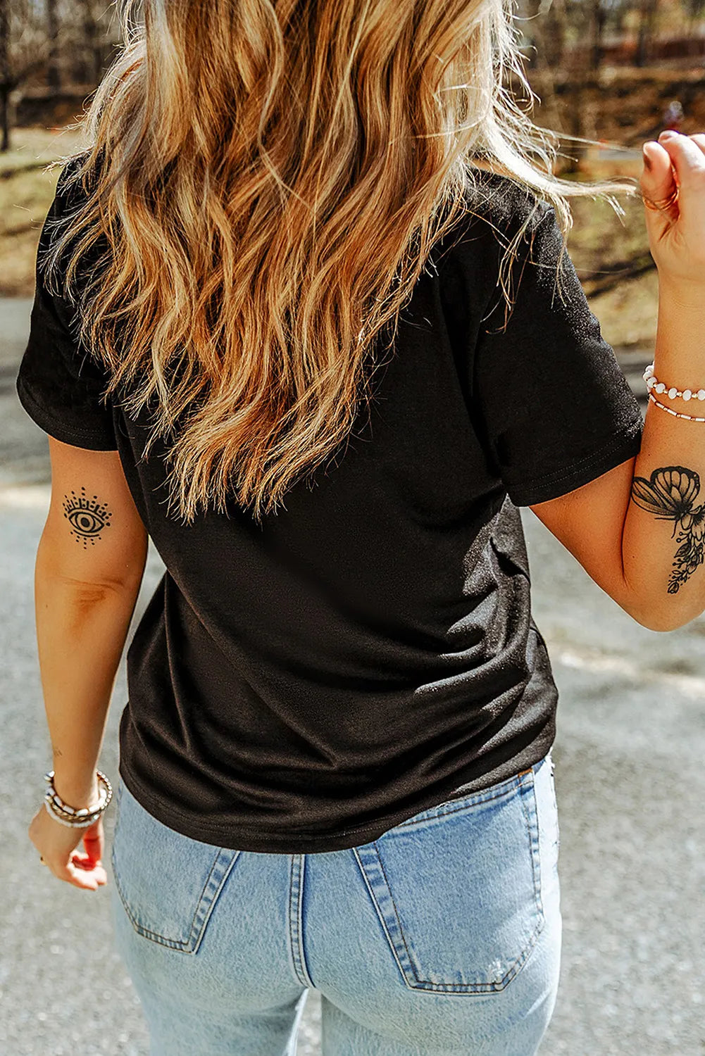 A woman from behind wears a black short-sleeve t-shirt and light blue jeans.