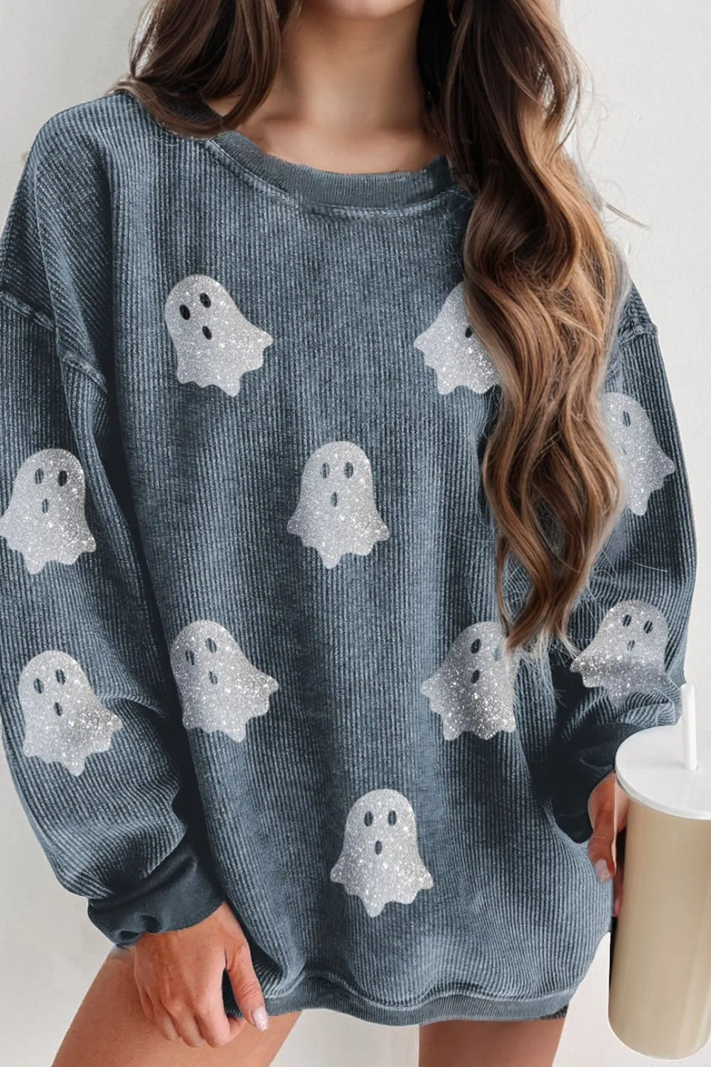 A woman wears a blue corduroy long-sleeve sweatshirt with glitter ghost appliques.