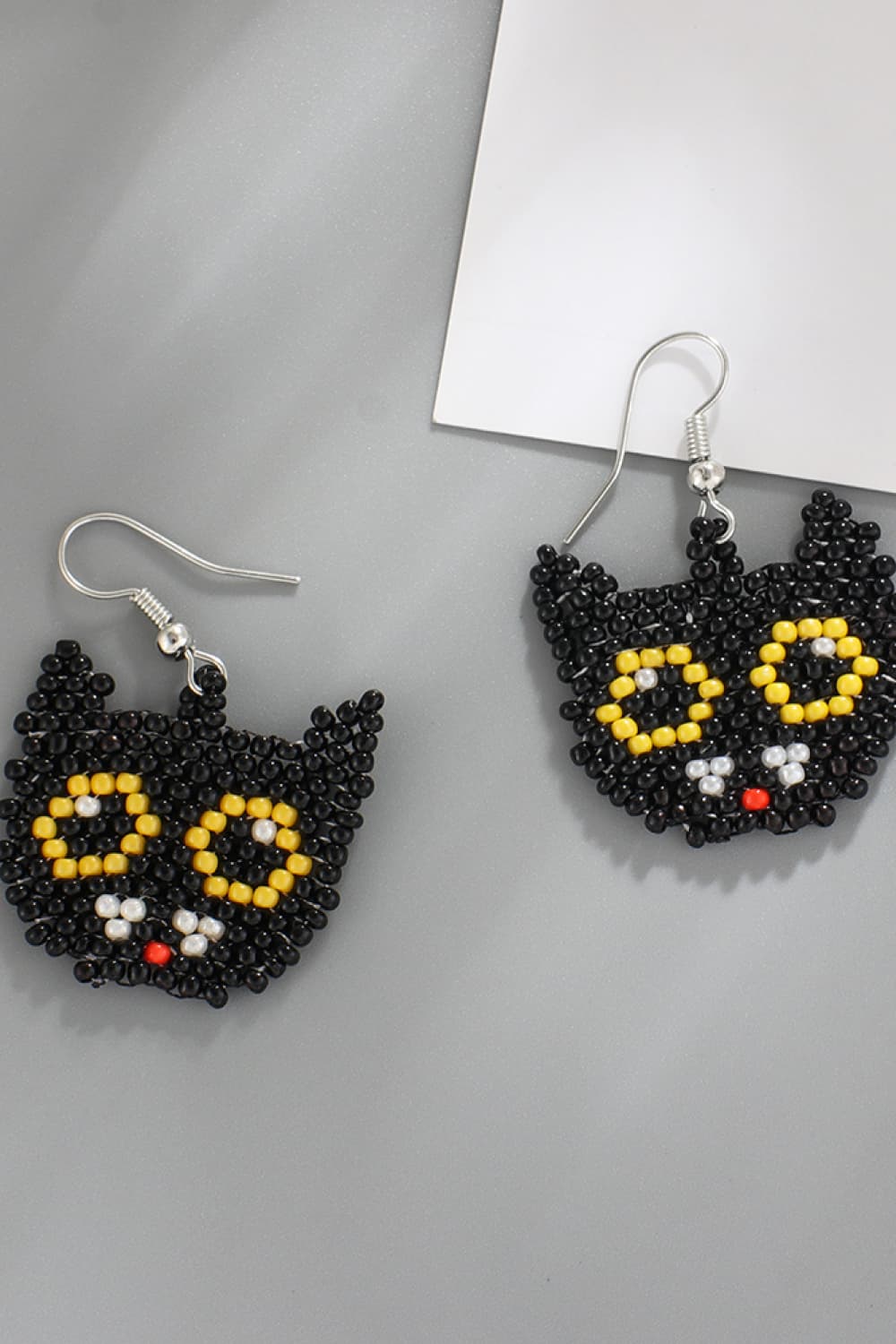Two black beaded cat-shaped earrings with yellow eyes, white pupils, and a red nose.
