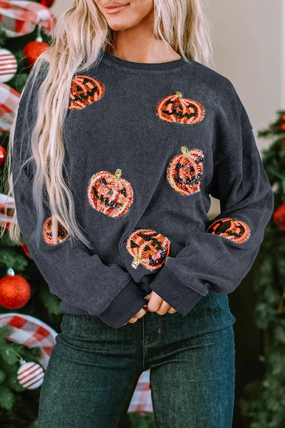 A woman wears a dark gray sequin patch pumpkin round neck sweatshirt and dark jeans.