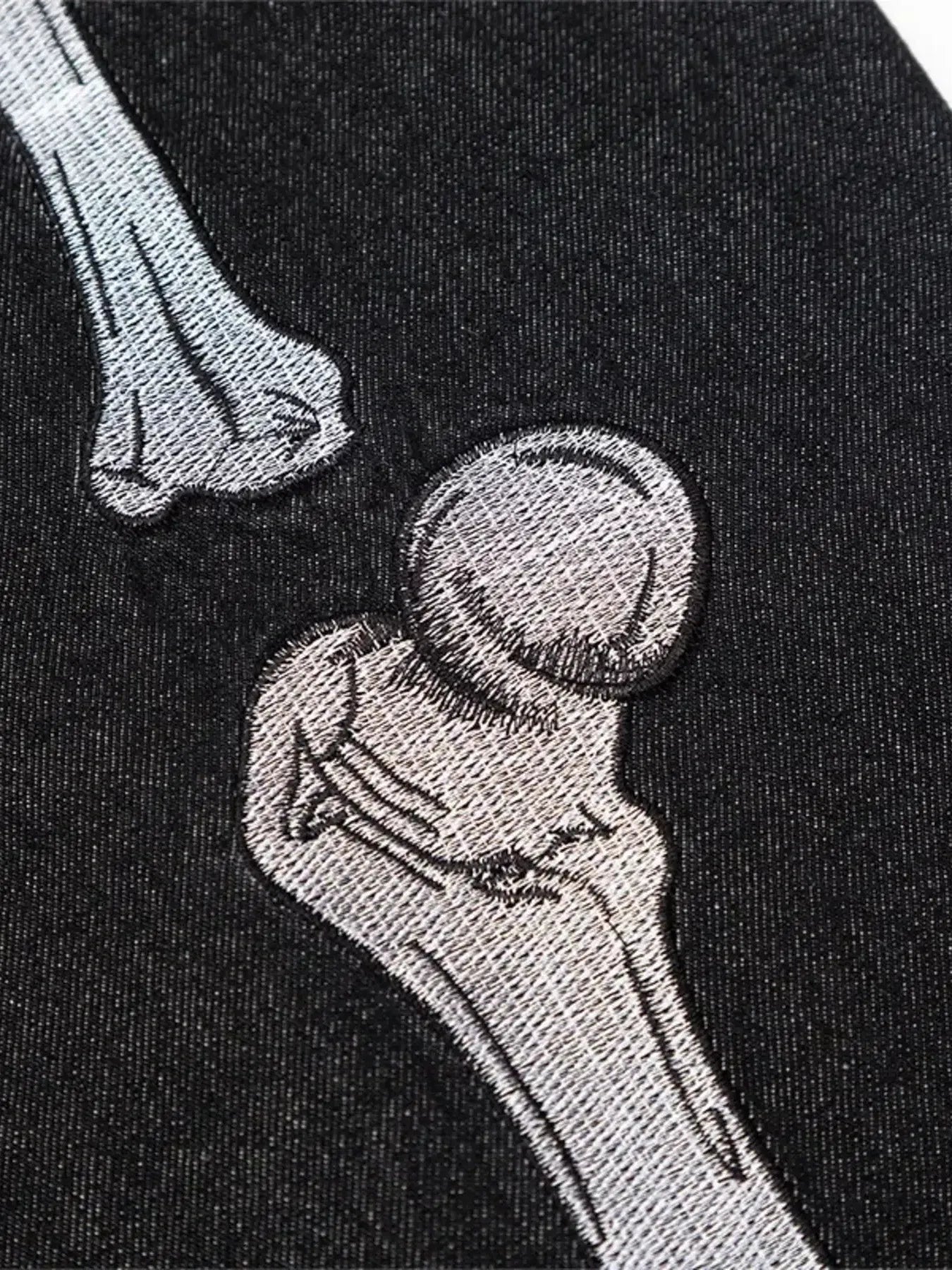 Close-up of embroidered skeleton bones on black denim.