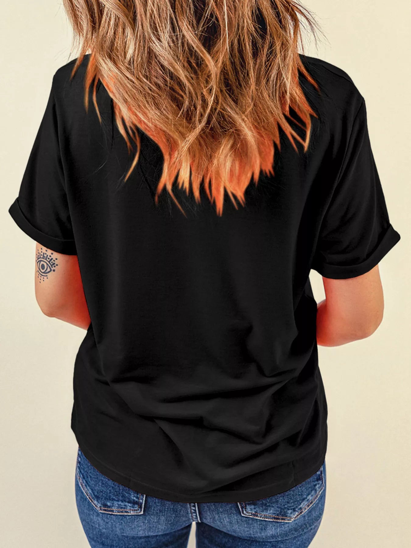 A woman with long, wavy hair wears a black t-shirt and blue jeans.