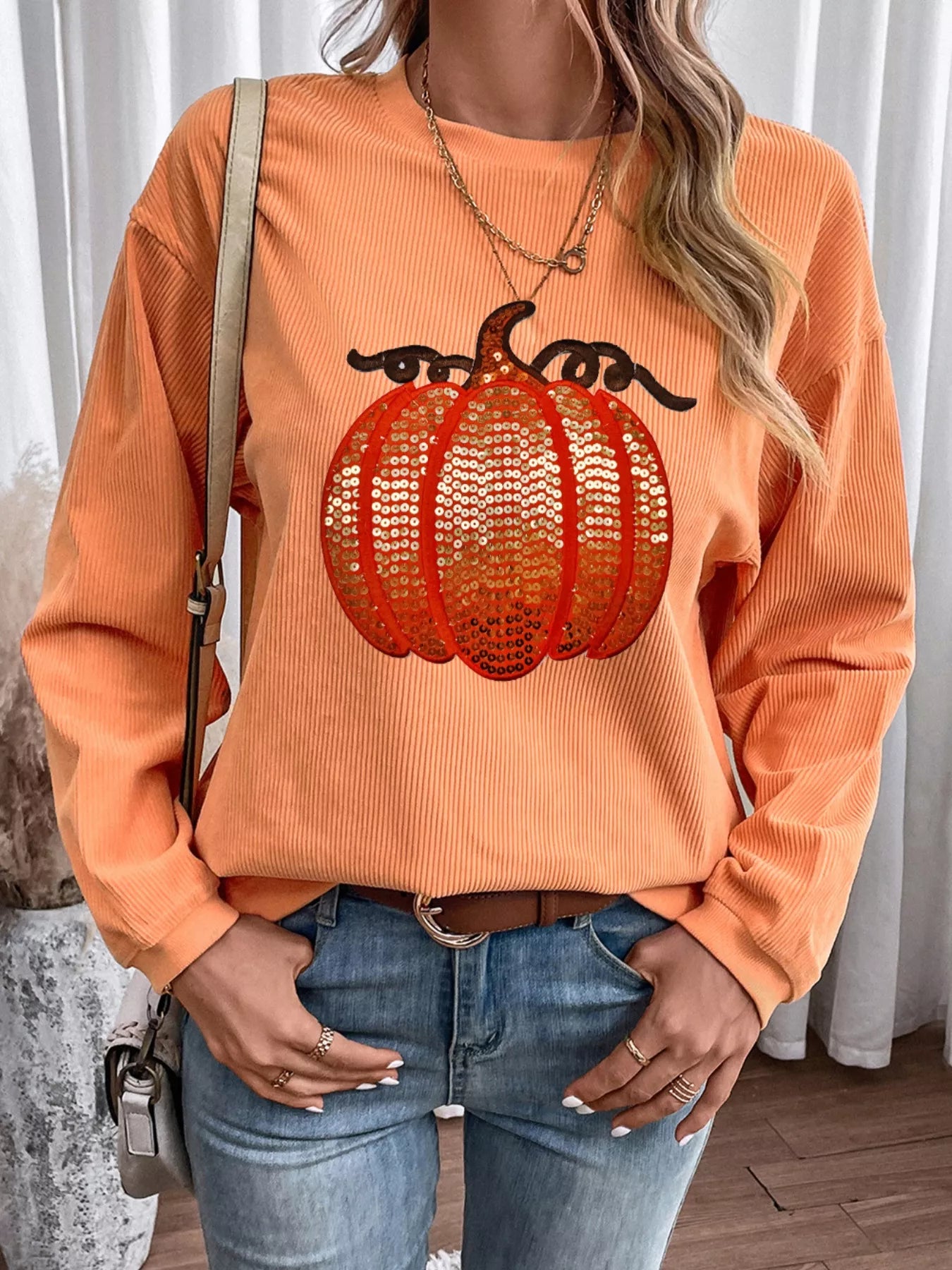 A woman wears an orange ribbed sweatshirt with a sequined pumpkin design.