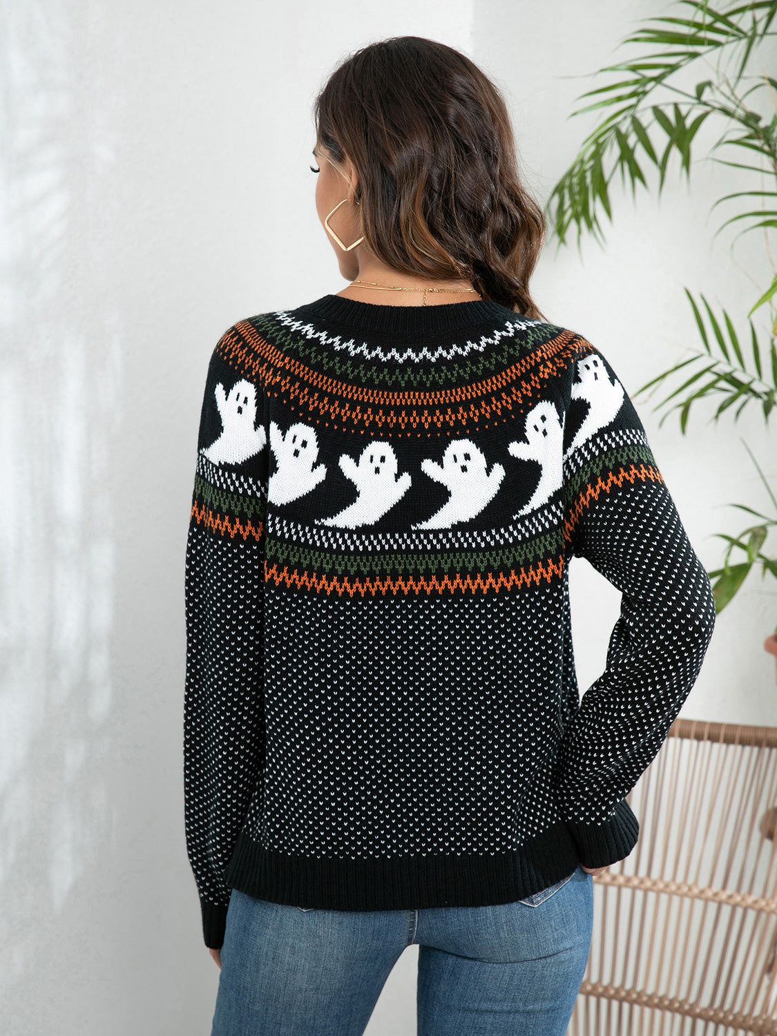 A woman from behind wears a black, orange, and green ghost-patterned sweater.