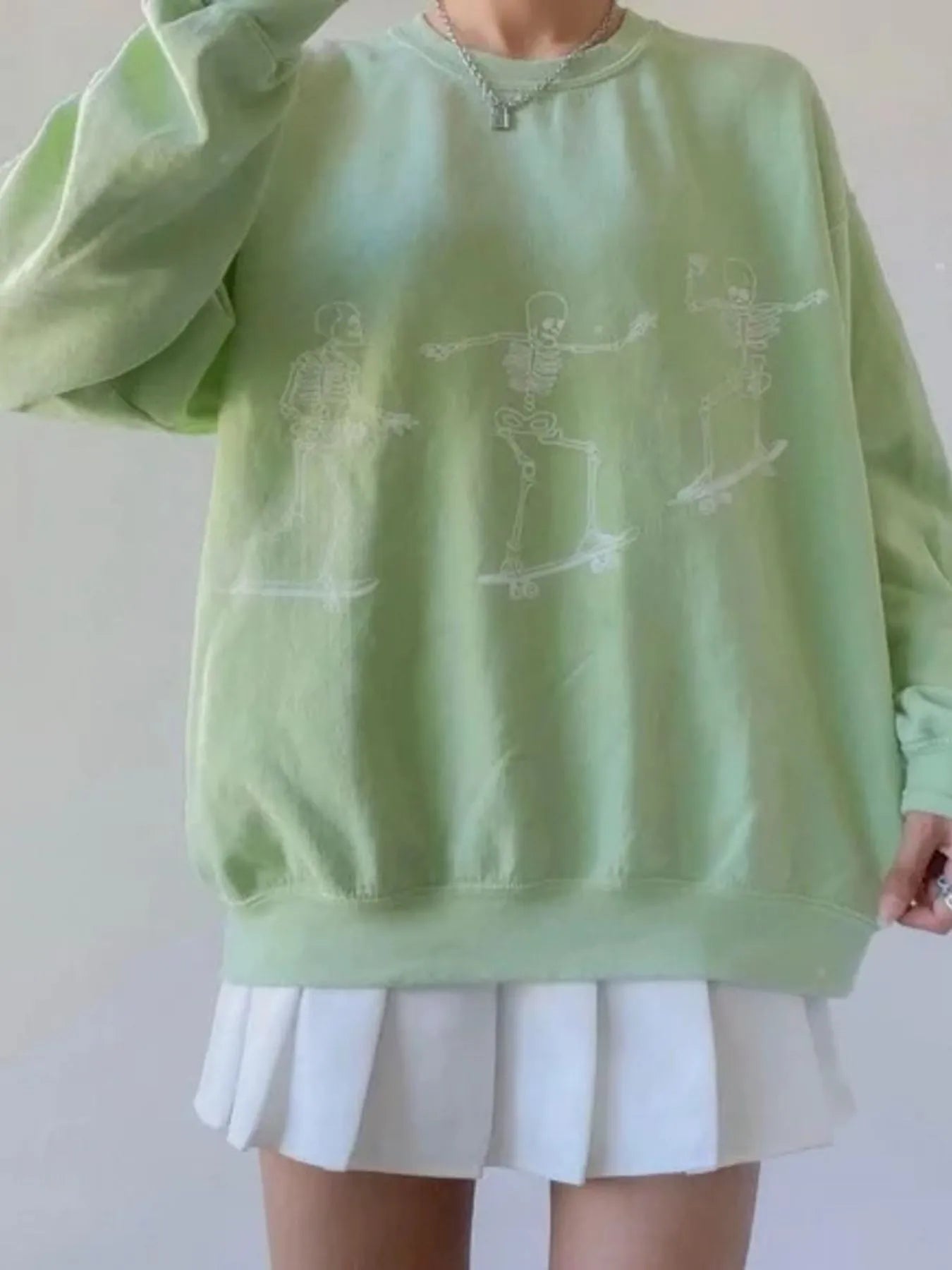 Oversized light green sweatshirt with white skeleton graphics and a white pleated skirt.
