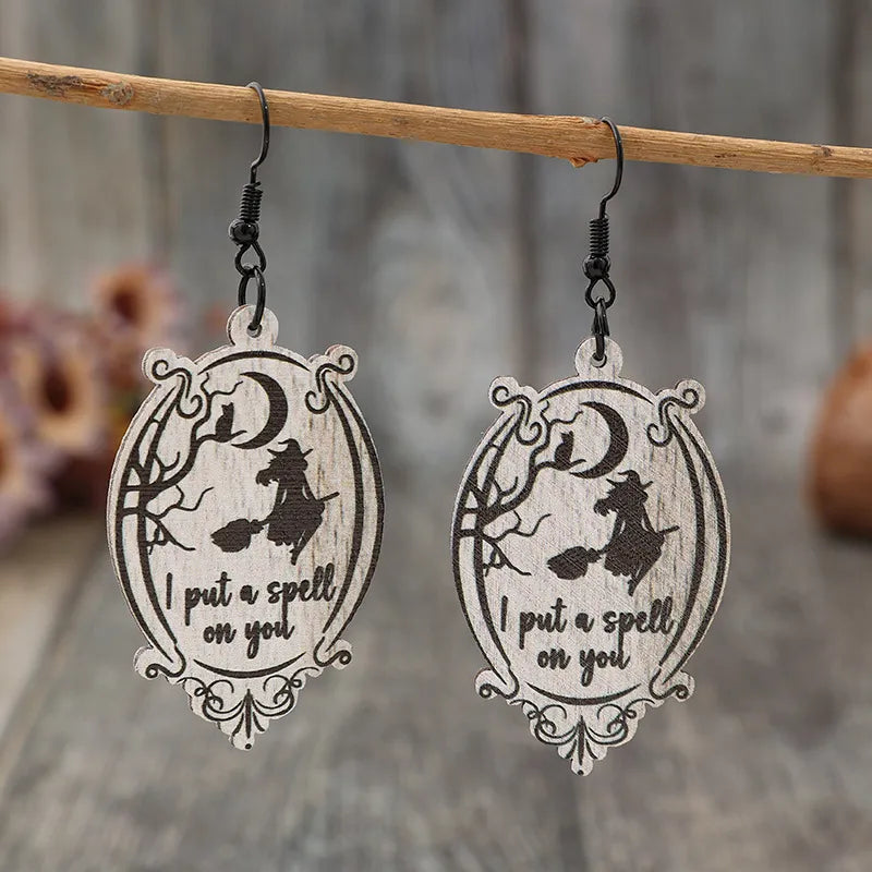 Two wooden dangle earrings feature a witch on a broomstick and the phrase "I put a spell on you."
