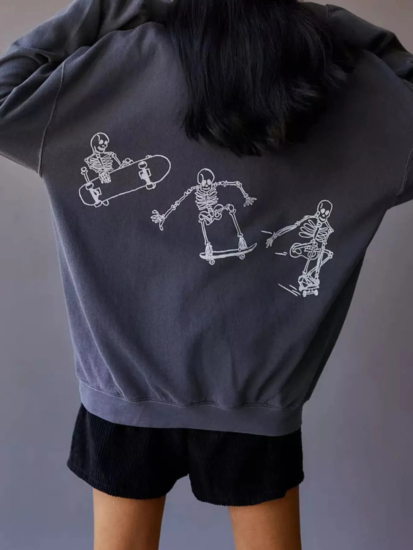 An oversized gray sweatshirt with three white skeleton graphics skateboarding on the back.