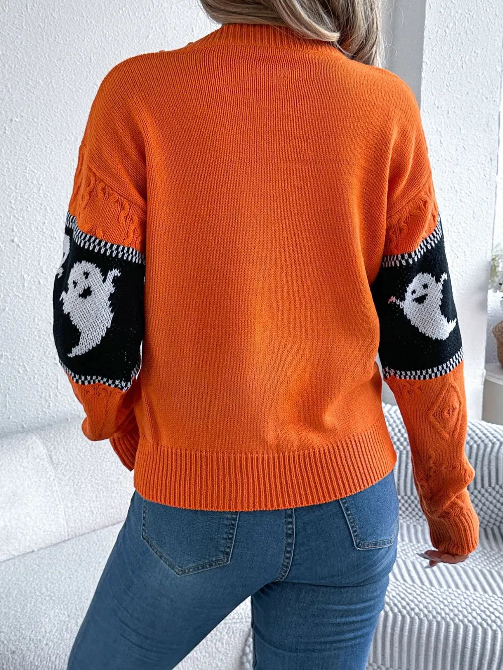 Orange long-sleeve sweater with white ghost designs on black arm panels.