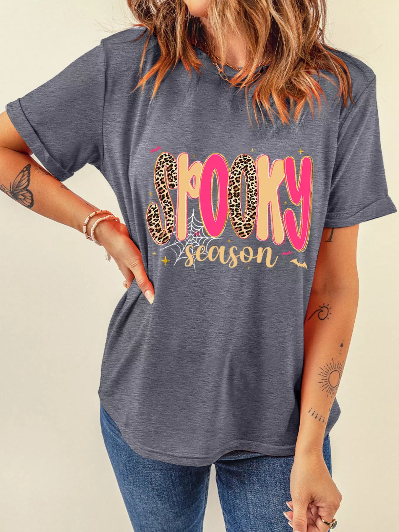 A woman wears a gray "Spooky Season" graphic t-shirt with leopard print and pink letters.