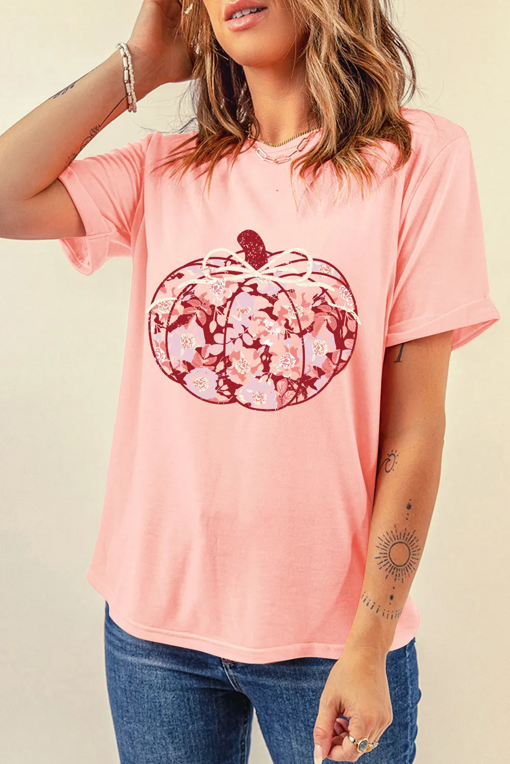 A woman wears a pink short-sleeve t-shirt with a floral pumpkin graphic.