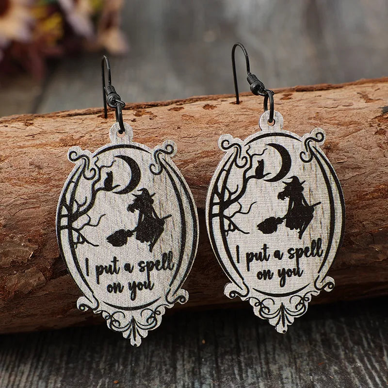 A pair of wooden dangle earrings featuring a witch on a broomstick and the text "I put a spell on you."