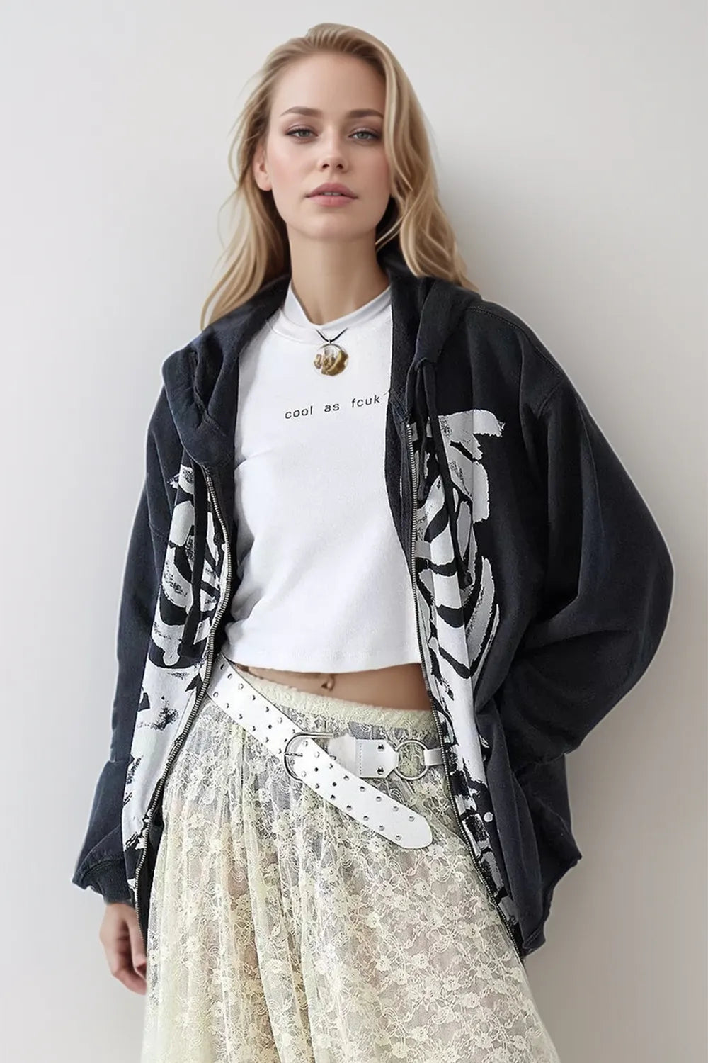 A woman wears a black skeleton zip-up hoodie over a white crop top and lace skirt.