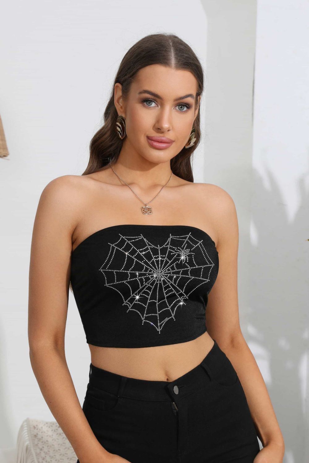 A woman models a black tube top with a rhinestone heart spider web graphic.